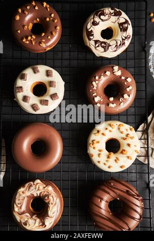 Vertikale Aufnahme von köstlichen Donuts in der weißen und bedeckt Braune Schokoladenglasur auf einem schwarzen Tisch Stockfoto