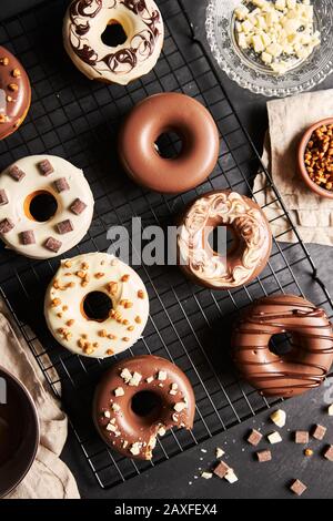 Vertikale Aufnahme von köstlichen Donuts in der weißen und bedeckt Braune Schokoladenglasur auf einem schwarzen Tisch Stockfoto