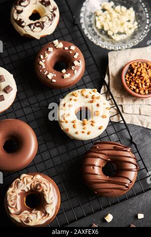 Vertikale Aufnahme von köstlichen Donuts in der weißen und bedeckt Braune Schokoladenglasur auf einem schwarzen Tisch Stockfoto