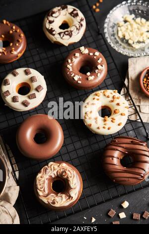 Vertikale Aufnahme von köstlichen Donuts in der weißen und bedeckt Braune Schokoladenglasur auf einem schwarzen Tisch Stockfoto