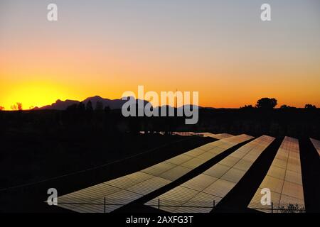 Solar Power in the Desert - Silhouette von Kata Tjuta bei Sonnenuntergang auf dem Tjintu Solar Field, Sails Resort Uluru erneuerbare Energie aus Solarpaneelen Stockfoto