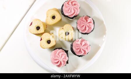 Schokoladenkuchen mit Himbeer-Buttercreme-Aufschäumen und herzförmigen Plätzchen schließen sich auf weißem Hintergrund, Draufsicht. Stockfoto