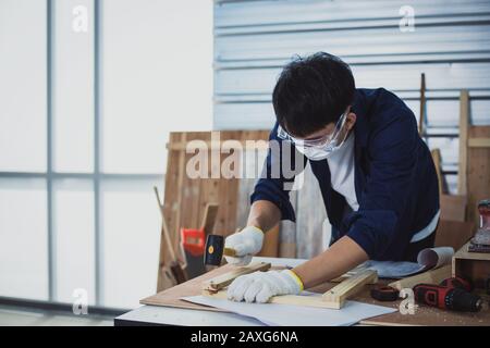 Asian man Carpenter arbeitet mit technischem Zeichnen oder Baupapier, das auf einer Werkstatt mit Zimmermannswerkzeugen und Holz zu Hause liegt Stockfoto