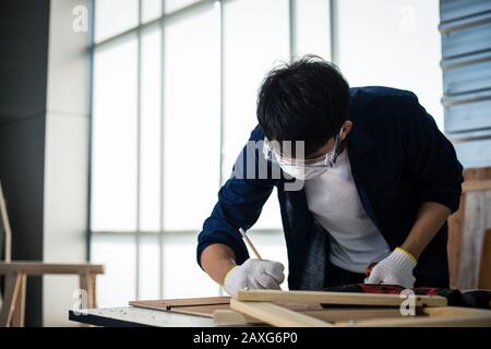 Asian man Carpenter arbeitet mit technischem Zeichnen oder Baupapier, das auf einer Werkstatt mit Zimmermannswerkzeugen und Holz zu Hause liegt Stockfoto