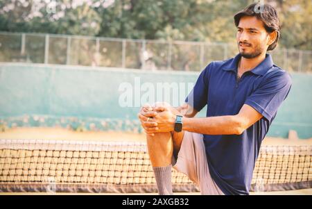 Der junge Tennisspieler streckt sich die Beine, bevor er auf dem Tennisplatz spielt - das Konzept, sich aufzuwärmen, bevor er Sport treiben kann. Stockfoto