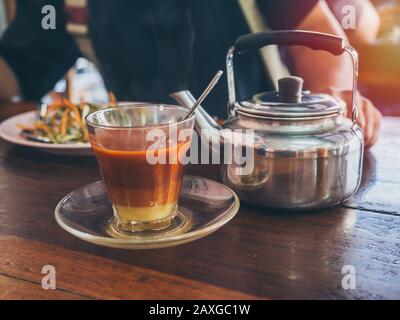 Frühstück im thailändischen Südstil, heißer thailändischer Tee aus Glas und ein alter Wasserkocher am Morgen auf Holztisch. Stockfoto