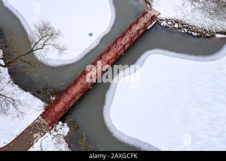 Leere Holzfußgängerbrücke über gefrorenen Fluss im Winter bewölkt, Luftdronfoto Stockfoto