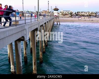 Viele Touristen, die während des Sonnenuntergangs auf dem Huntington Beach Pier spazieren, mit Blick auf die Stadt und den Strand. Stockfoto