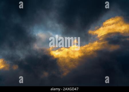 Atemberaubende, flauschige Gewitterwolken, die bei Sonnenuntergang durch verschwindende Strahlen und dunkle Gewitterwolken, die über den Himmel schweben, beleuchtet werden, um das Wetter in der Saison zu ändern Stockfoto