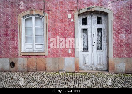 Schöne weiße Tür umgeben von rosafarbenen Fliesen in Silves, Portugal, mit Kopfsteinpflaster Stockfoto