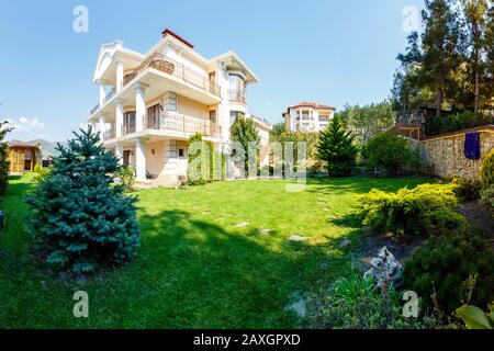 Der Hinterhof eines weißen dreigeschossigen Cottages mit Säulen und schmiedeeisernem Geländer, italienischer Stil, klassisch. Grüner Garten, Rasen und leerer Pool in Fron Stockfoto