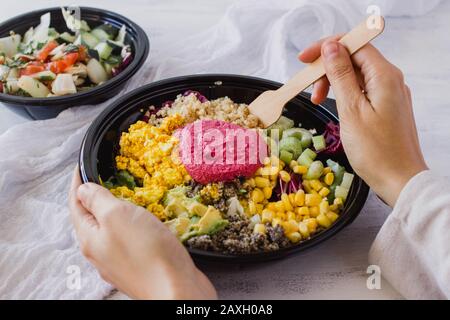 Buddha-Schüssel-Konzept für gesundes Essen. Veganer Detox-Salat mit Quinoa und Rübenhummus auf weißem Hintergrund. Instagram-Stil mit den Händen, die essen Stockfoto