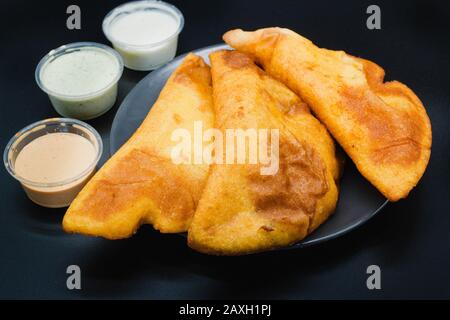 Empanadas venezolanas auf schwarzem Hintergrund mit verschiedenen Soßen wie Guasacaca und würziger Soße. Empanada aus Venezuela wird gebraten und mit Mais hergestellt Stockfoto