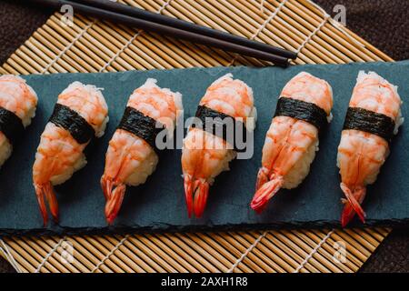 Nigiri sushi bereit, auf einem Schiefer mit Essstäbchen und einer traditionellen Bambusrollmatte zu essen Stockfoto