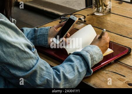 Frau Enterpreneur sucht auf dem Smartphone und schreibt die Informationen auf Stockfoto