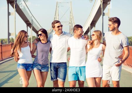 Im Sommer geht eine fröhliche Gruppe von Freunden und Freundinnen über die Brücke und macht Spaß Stockfoto