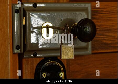 Ein Schlüssel mit einem kleinen Vorhängeschloss am Ende ist in einem Schlüsselloch auf einem Pfriemschloss an einer Holztür eingesetzt