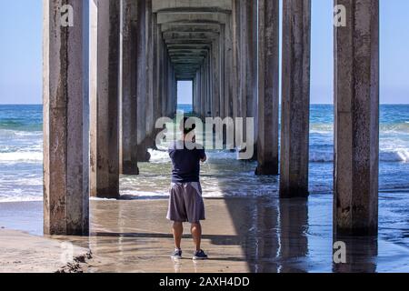 Ein junger Mann, der unter dem Betonsteg in San Diego, Kalifornien, Bilder vom Ozean machte Stockfoto