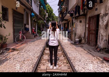 Asiatisches Touristenmädchen in einer weißen Bluse und schwarzen Hosen, die inmitten einer Train Street, Hanoi Vietnam, fotografieren. Stockfoto