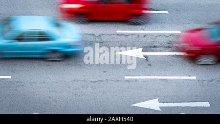 Rotes und blaues Auto bewegt sich schnell auf Asphaltstraße in der Stadt. Verschwommene Bewegung des schnellen Kompaktwagens auf Asphaltstraße. Stadtverkehr mit Hauptverkehrszeit Stockfoto