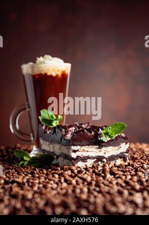 Köstlicher Schokoladenkuchen mit Minze und Kaffeegetränk mit Sahne. Kaffeebohnen sind auf dem Tisch verstreut. Kopierbereich. Stockfoto