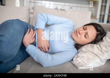 Frau, die auf einem Sofa liegt und einen Magenschmerzen hat Stockfoto