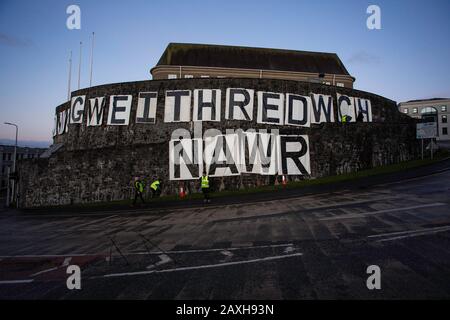 Carmarthen, Großbritannien. Februar 2020. Mitglieder des Extinction Rebellion in Carmarthen entfachen Banner, die "Act Now" ("Gweithredwch Nawr" auf walisisch) auf den Seiten der County Hall in Carmarthen lesen. Kredit: Gruffydd Ll. Thomas/Alamy Live News Stockfoto