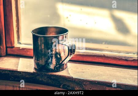 Der alte Metallbecher steht auf einem Holzfensterschweller Stockfoto