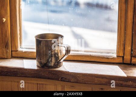 Der alte Metallbecher steht auf einem Holzfensterschweller Stockfoto