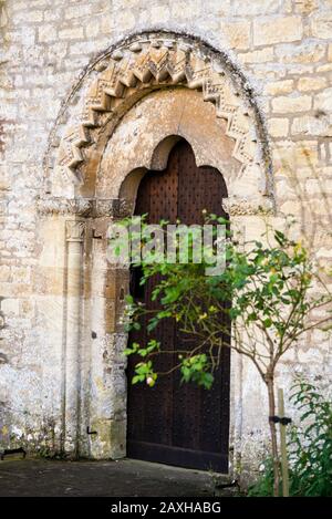 Normannisch geschnitzte Tordurchfahrt in der St. Mary's Saxon Church in Bibury England, mit einem einfarbigen Tympanon, das geschnitten wurde, um ein Baumfolienmuster zu erzeugen. Stockfoto