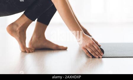 Frau rollt auf dem Holzboden im Studio eine Yogamatte Stockfoto