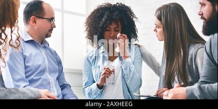 Mitglieder Der Therapy Session Group Trösten Weinende Frau Und Geben Glas Wasser Stockfoto