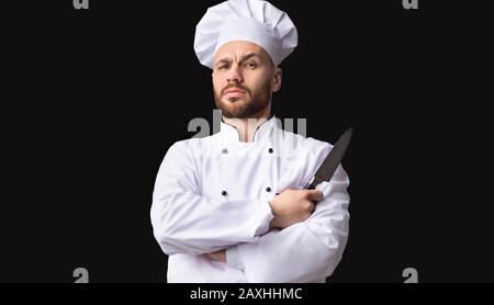 Ernst Chef Holding Knife Betrachtet Camera Posing, Studio Shot Stockfoto