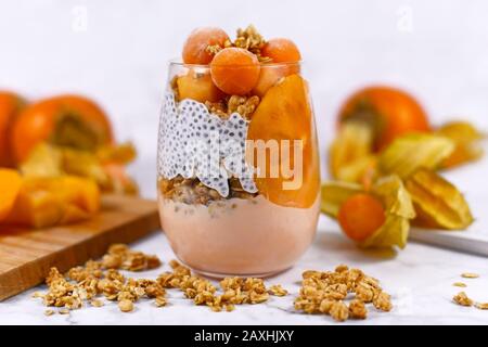 Gesundes Frühstück auf 2 Ebenen in Glas mit chia Seeds Pudding, gemischt mit Granola und mit orangefarbenem Persifmon und Physalis Stockfoto