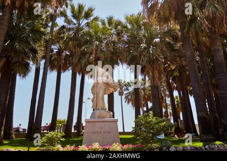 Cannes, FRANKREICH - 06. Juni 2019: Statue der Jeanne D'Arc in Cannes Frankreich an einem strahlend wolkenlosen sonnigen Tag mit Palmen, die hoch hinter ihr stehen. Stockfoto