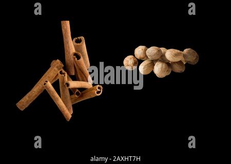 Frieren Sie die Bewegung der fliegenden Gruppe von Cinnamon Stick und ganzen Muskatsamen isoliert auf schwarzem Hintergrund ein. Stockfoto