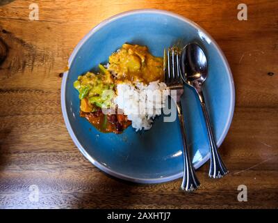 Draufsicht von indischem Curry und Reis auf einem Blauer Teller mit Löffel und Gabel auf einem hölzernen gesetzt Tabelle Stockfoto