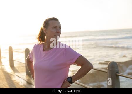 Seitenansicht einer kaukasischen Frau, die an einem sonnigen Tag an einer Promenade arbeitet und sich auf das Workout vorbereitet und die Aussicht bewundert Stockfoto