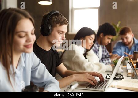 Student Guy tippt auf Laptop, studiert in Bibliothek Stockfoto