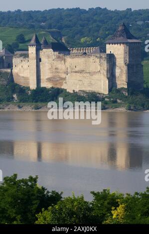 Festung Khotyn aus der Ferne - vom gegenüberliegenden Ufer des Dniester River. Grünes Laub im Vordergrund. Stockfoto