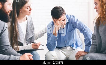 Depressiver süchtiger Mann, der bei einer Therapiesitzung Unterstützung von Gruppenmitgliedern erhält Stockfoto