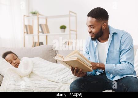 Afrikanischer Papa liest Buch für seine schlafende Tochter Stockfoto