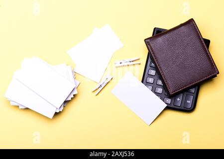 Ledertasche, Taschenrechner und Karten auf gelbem Hintergrund. Konzept für Business-Zubehör. Visitenkarten mit leerem Platz im Stapel und Holzkleidern. Briefpapier und Taschenrechner. Stockfoto