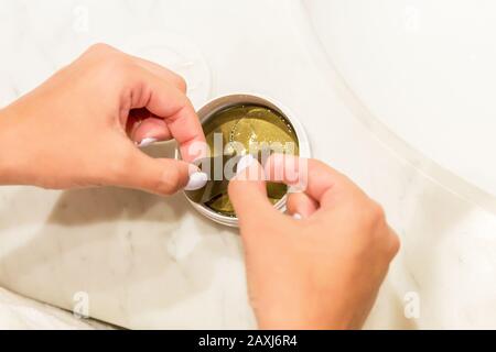 Weibliche Hände nehmen mit der Pinzette Augenflecken aus dem Behälter. Anti-Aging-Konzept. Stockfoto