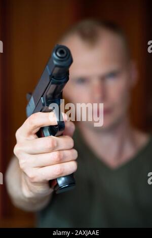 Ein Mann zielt auf seine halbautomatische Pistole. Selektiv auf die Vorderseite der Waffe fokussiert Stockfoto