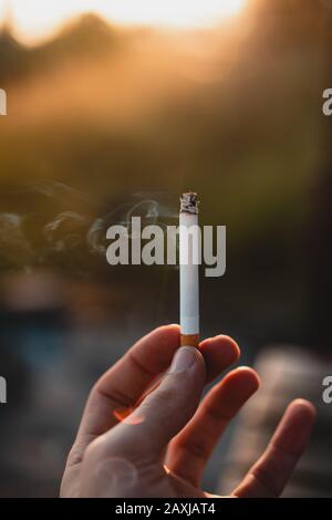 Person, die eine angezündete Zigarette in der Hand hält.Gesundheitseffekte des Zigarettenrauchens. Stockfoto