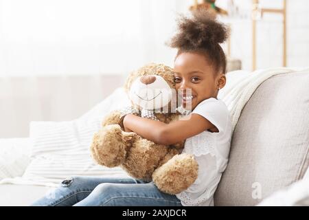 Glückliches schwarzes Mädchen umarmte Teddybär und posierte vor der Kamera Stockfoto