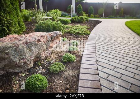 Dekorative Steine im Garten: Der geflieste Pfad in einem schönen Park führt unter sanfter Sonneneinstrahlung durch einen grünen Rasen. Stockfoto