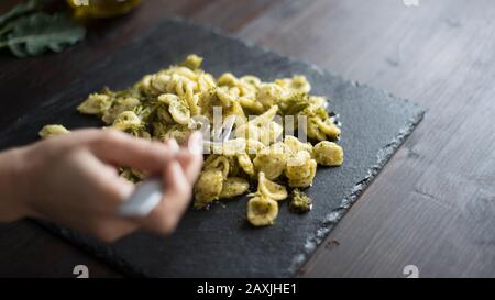 Nahaufnahme der Hand einer Frau, die mit einer glätterigen Gabel mit Brokkoli, einem typischen apulischen Rezept, in Hintergrundbeleuchtung auf dunklem Holztisch mit aufhebt Stockfoto