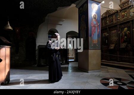 Ein Griechisch-orthodoxen Mönch steht an der mittelalterlichen Höhlenkirche im griechischen orthodoxen Heiligen Kloster des Berges Sarantarion oder Der Versuchung, die an den hängen des Berges der Versuchung erbaut wurde, die sich entlang einer Klippe mit Blick auf die Stadt Jericho in den palästinensischen Gebieten in der Nähe des Jordan im Westen befindet Bank, Israel Stockfoto